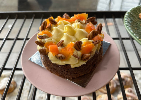 Small cake with white frosting, carrots, and nuts on a pink plate.